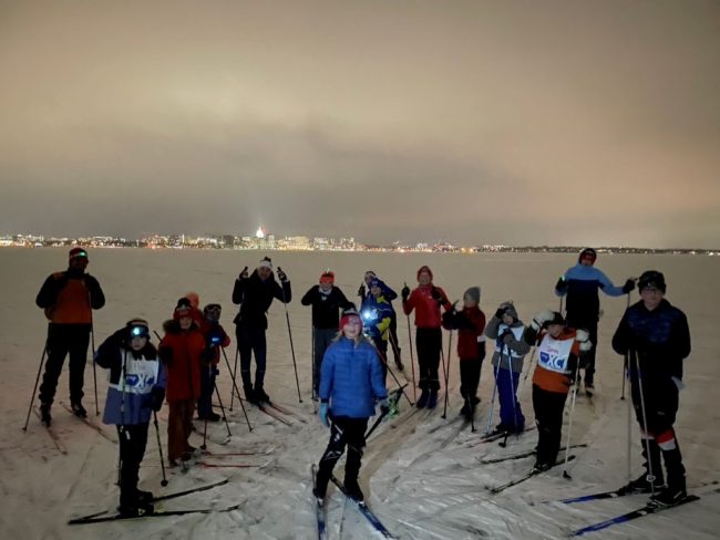 cross country skiiers on Lake Monona at night during their practice with a view of the Capitol building 