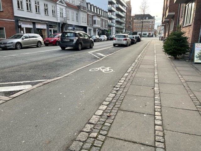 A city street in Copenhagen with infrastructure for vehicle traffic, parking, bike lane, and pedestrian walkway.	