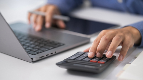 a person with their hands on a laptop and calculator