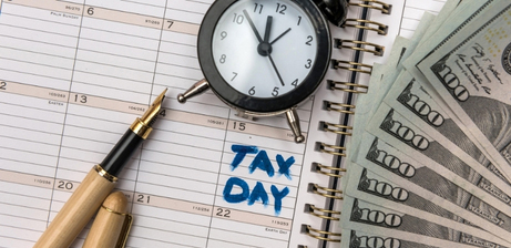 calendar with tax day circled, along with cash, a pen, and a clock
