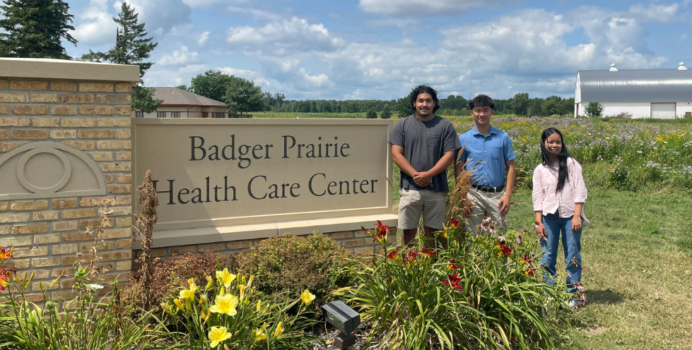 Three youths are standing near a sign that says Badger Prairie in a field.