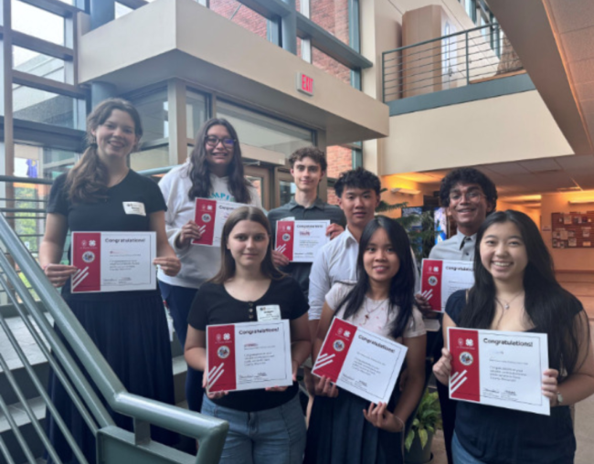 Eight young students pose for a photo holding their program completion certificates.
